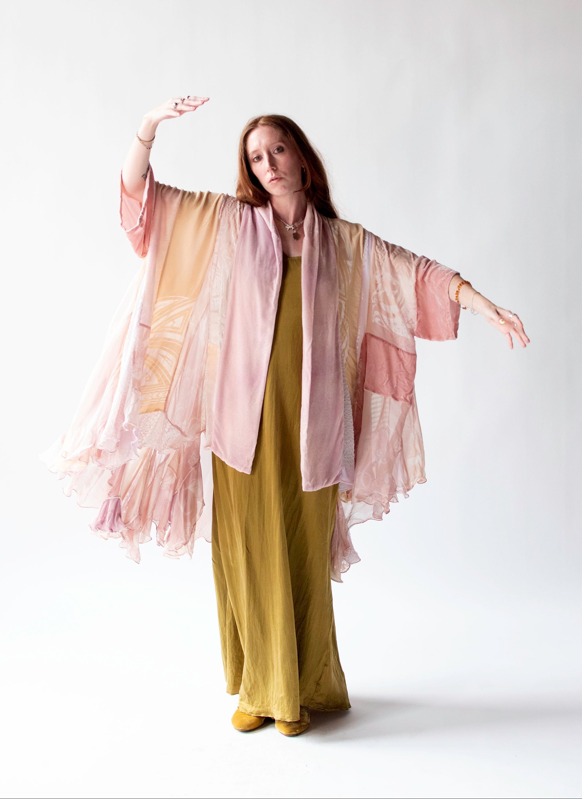 Woman wearing a long, light-colored kimono-style garment over a green dress on a white background